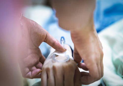 Cropped image of female nurse attaching IV drip on patient hand. Close-up of healthcare worker operating female. They are in hospital ward.